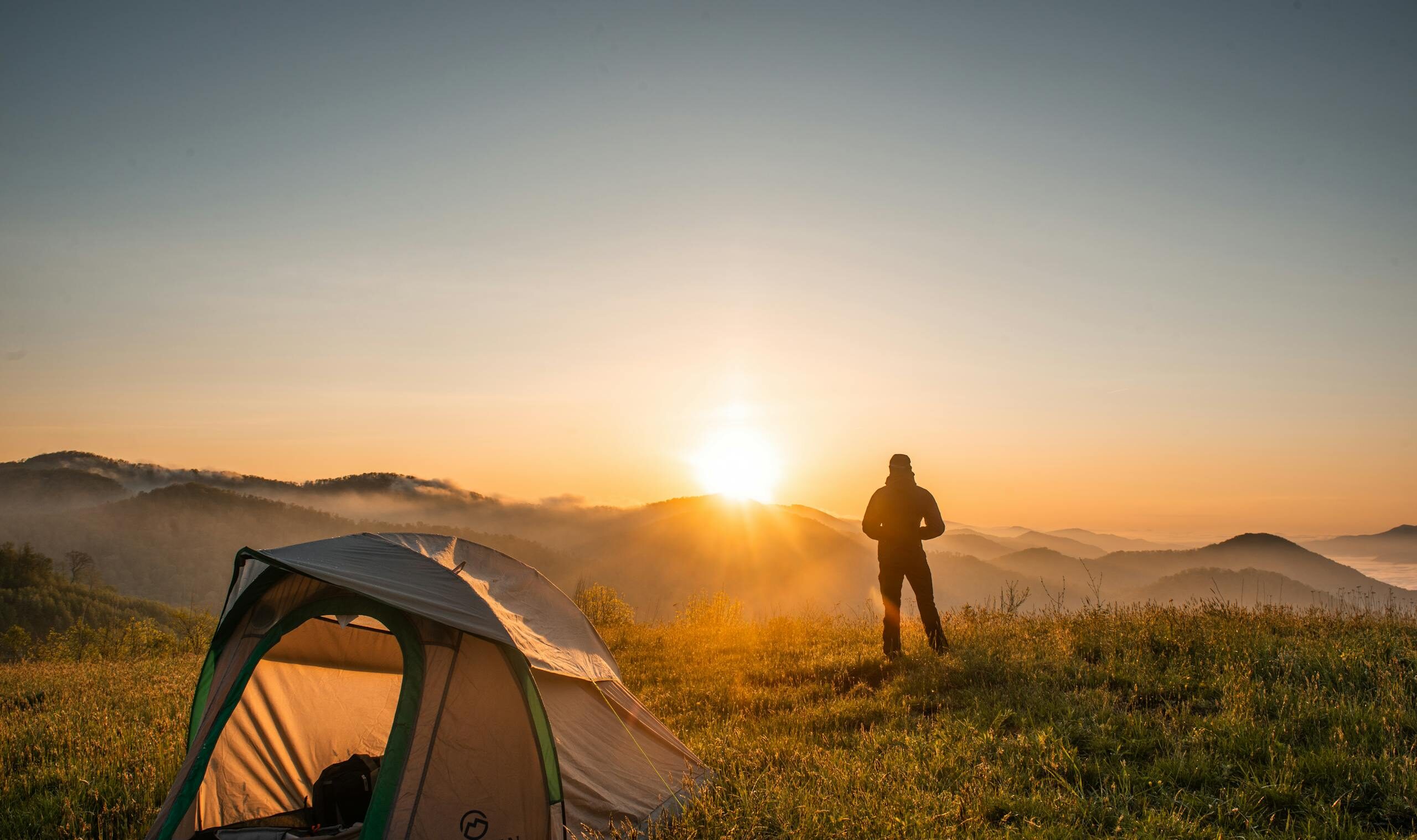 A camper enjoys the sunrise in a mountain setting with a tent. Perfect nature escape.