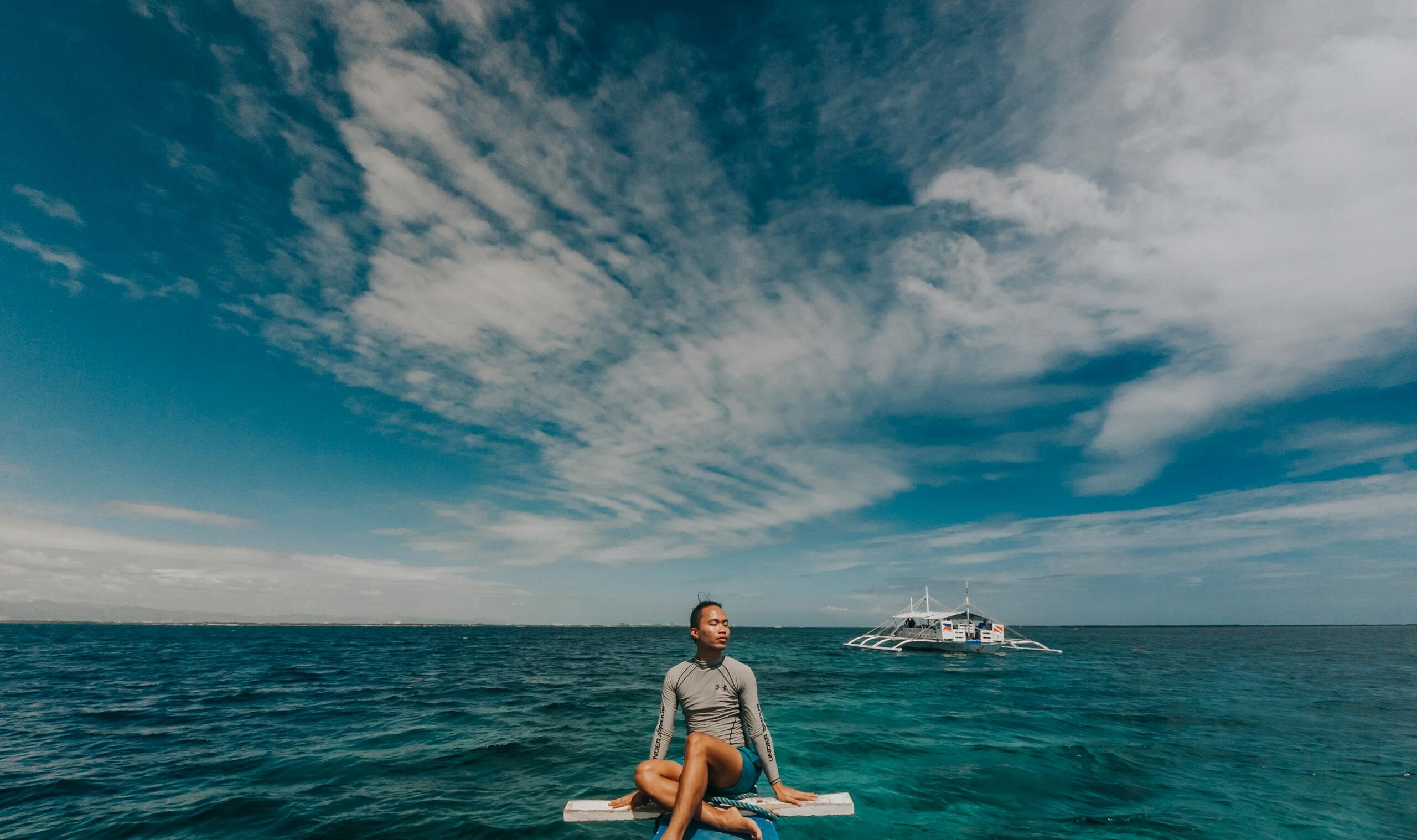 Man sitting on a boat's bow, enjoying a peaceful ocean view under a blue sky.