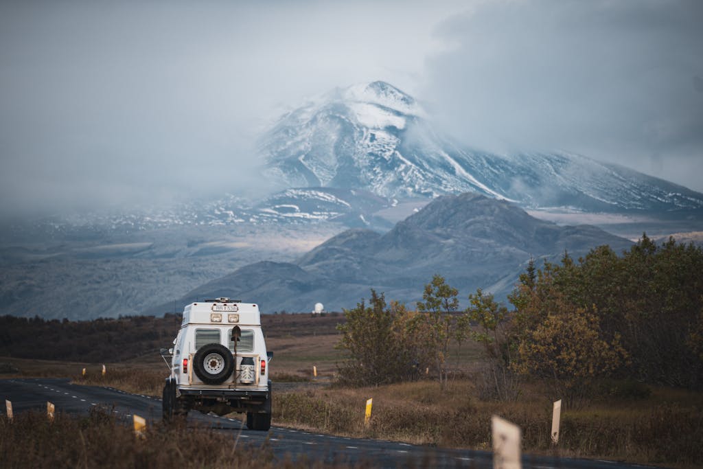 White SUV on rugged road with stunning snow-capped mountain view.