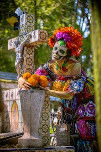 Colorful Catrina figure with floral offerings during Dia de los Muertos in Mexico City cemetery.